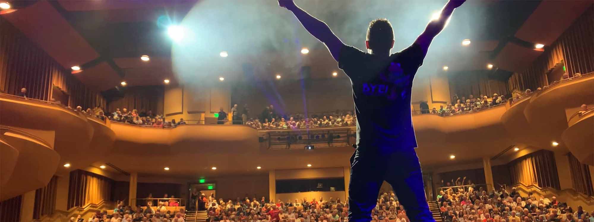 Dramatic photo of back of man with arms up in front of crowded Sharon theater